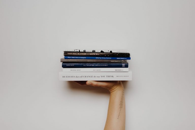 A person holds a pile of books stacked on top of one another